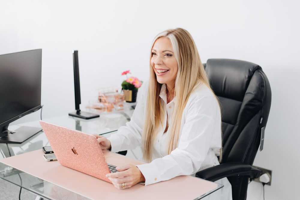Professional working at modern desk with pink laptop and computer monitor in bright office setting.