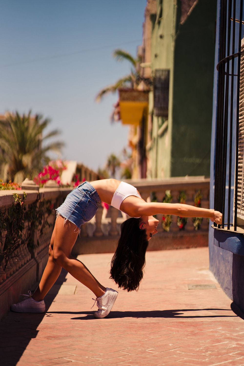 Athletic pose showing backbend on sunny terrace with palm trees in background.
