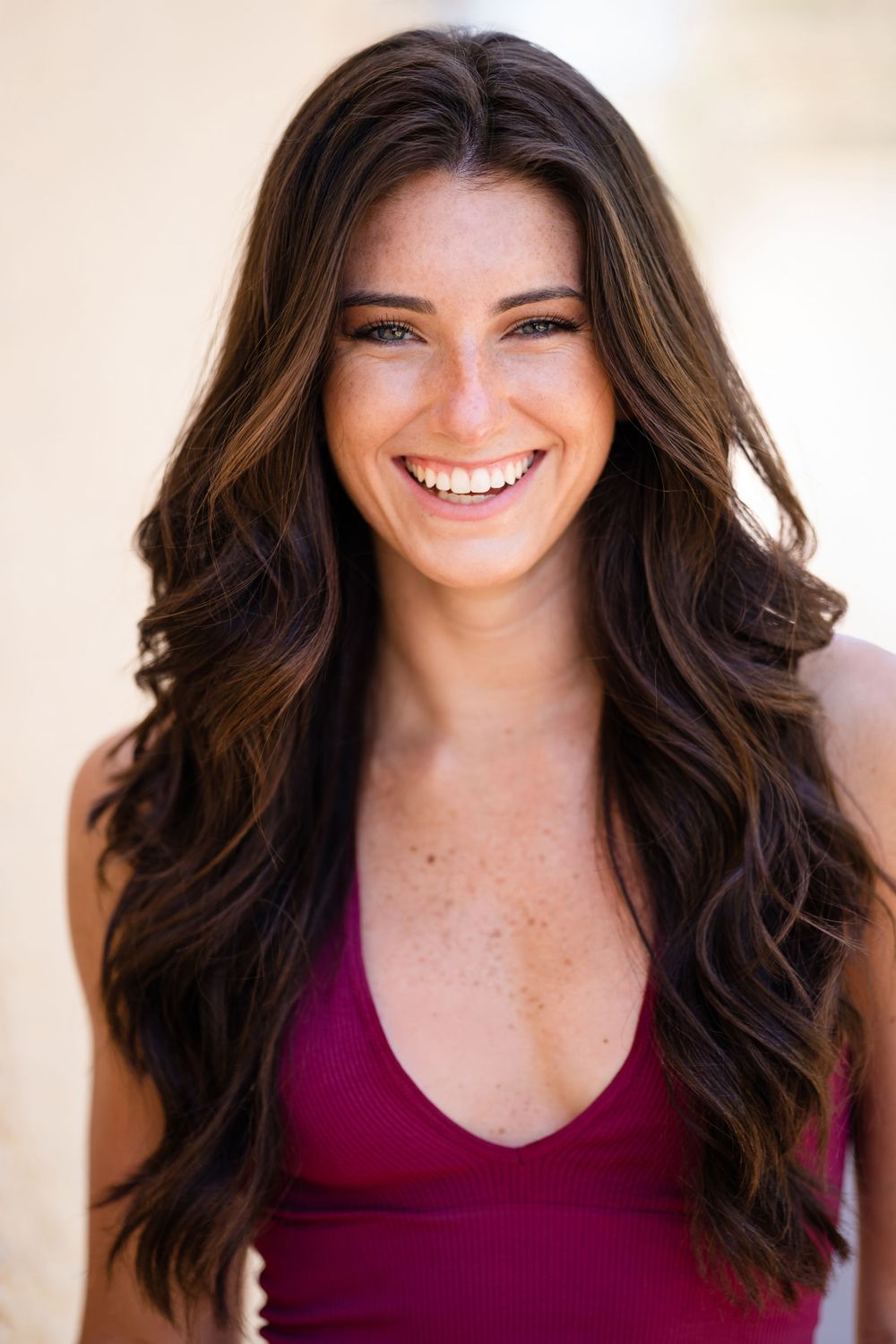 Portrait in burgundy tank top featuring flowing brown hair and natural makeup.