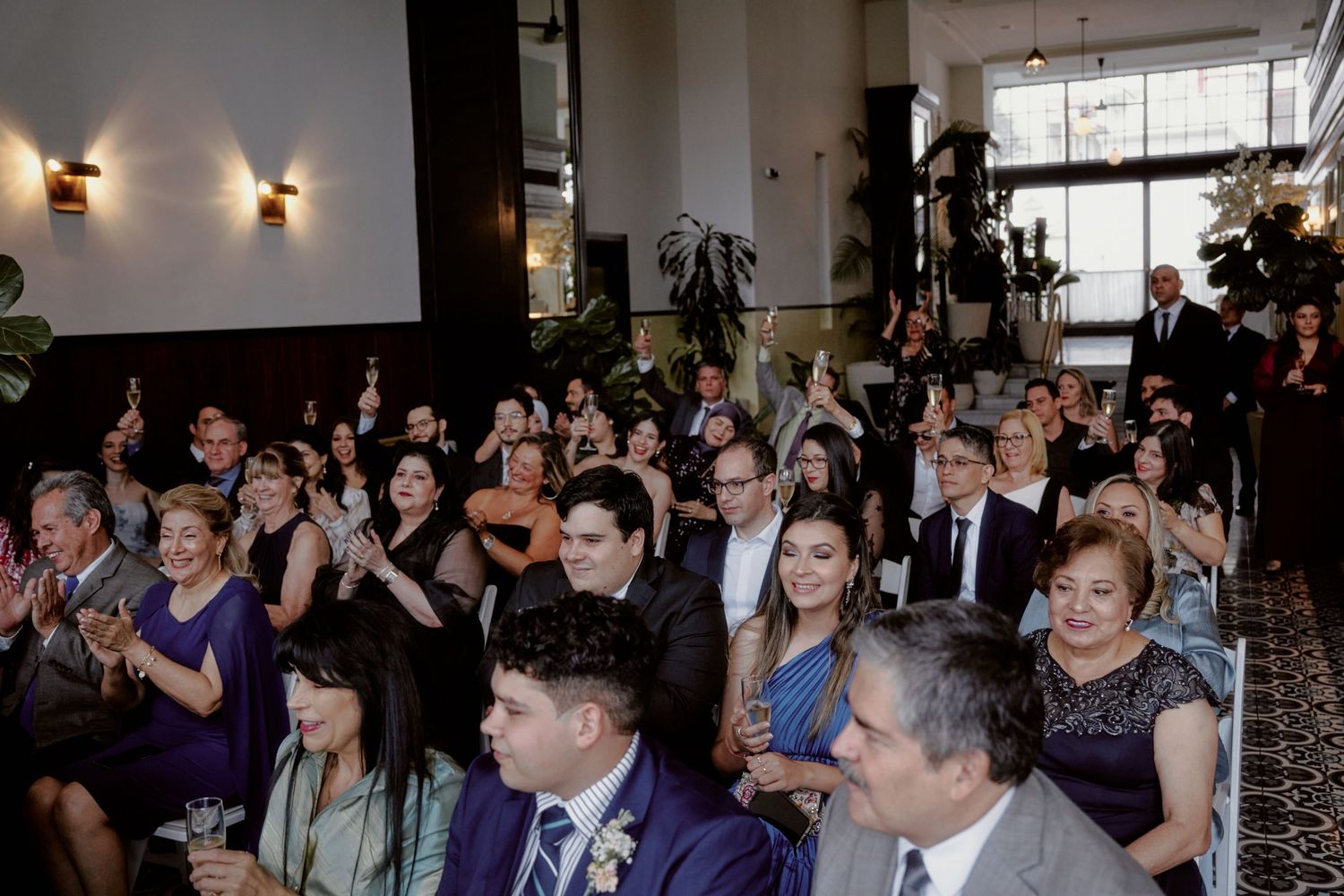 Wedding guests seated in rows during a ceremony in an elegant indoor venue with wall sconces.