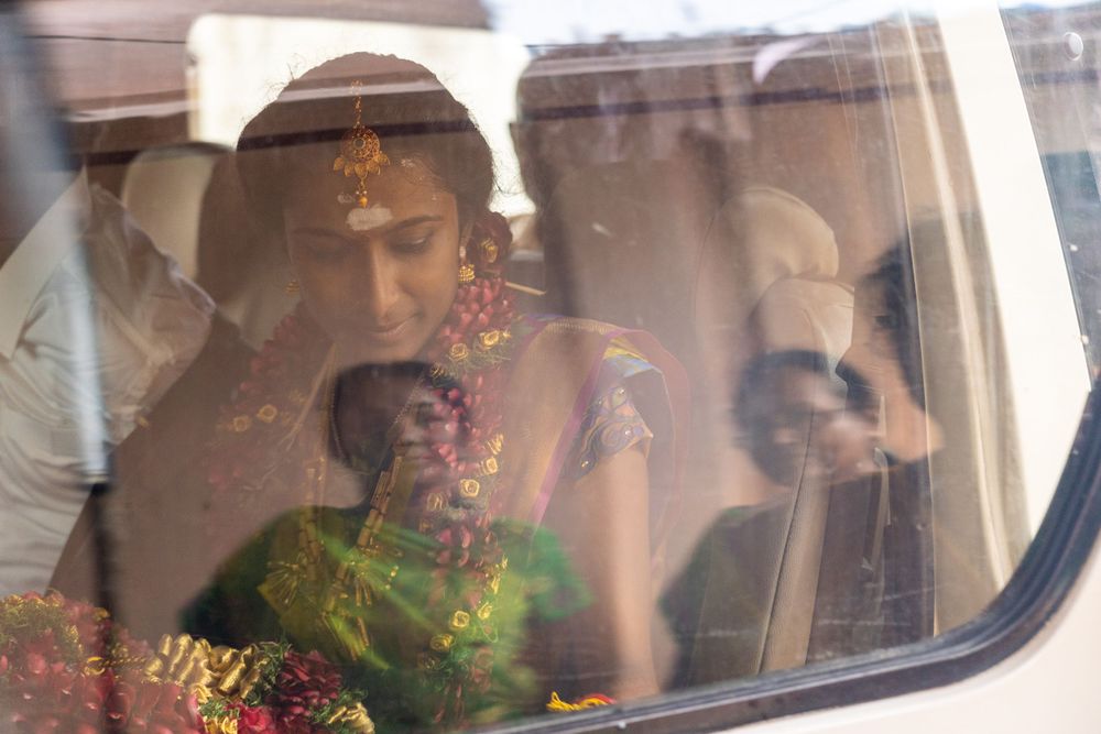 View through car window of person in traditional green attire with decorative garlands.