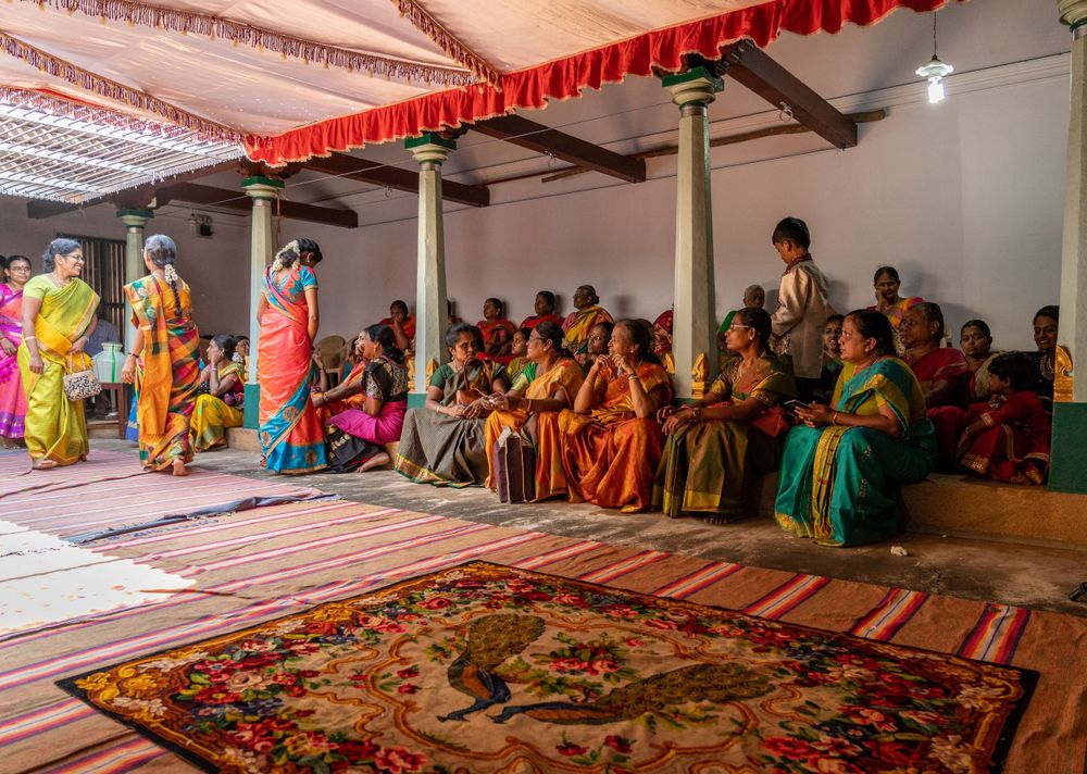 Guests in traditional Indian attire seated on floor during cultural ceremony with decorative carpet.