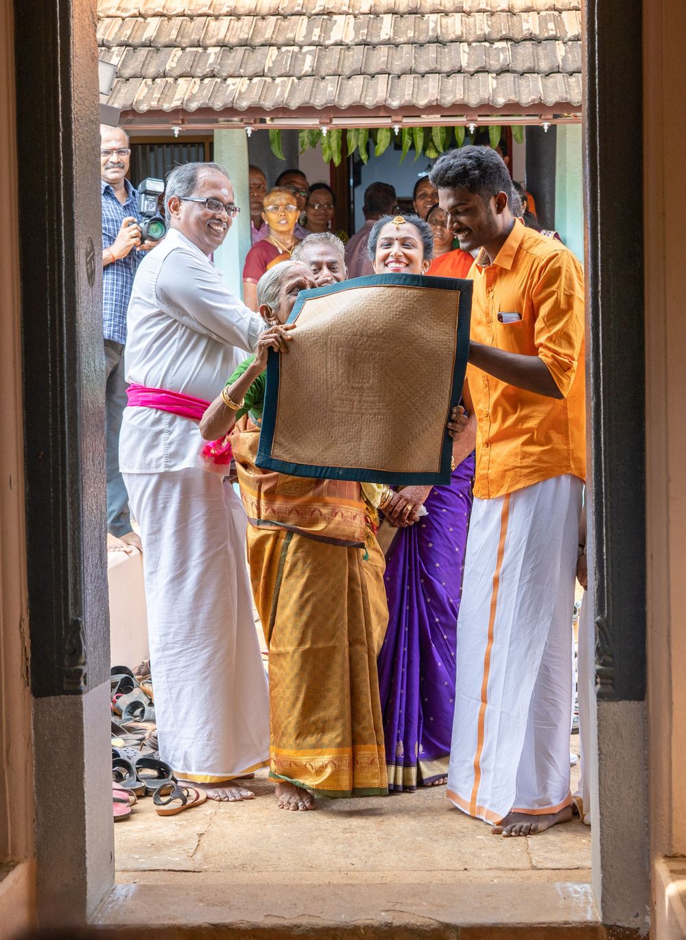Traditional Kerala ceremony with participants in white mundu examining a document through a doorway.
