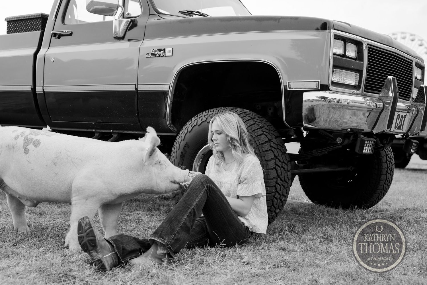 Black and white photo of someone sitting by a vintage truck with a white pig.