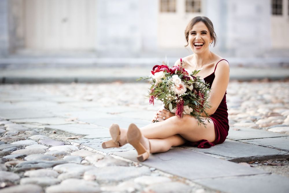 Ballet dancer sits gracefully on cobblestone holding a bouquet of flowers.