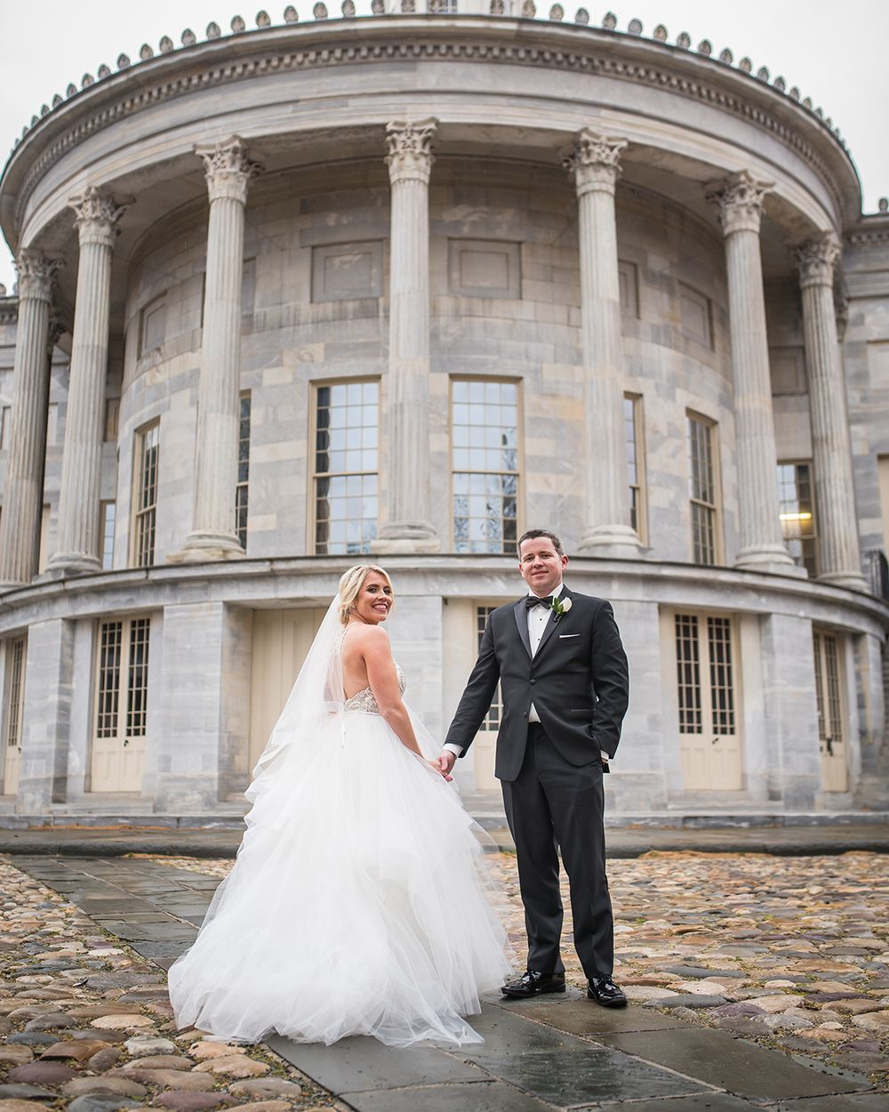 Wedding couple poses in front of a grand neoclassical building with columned architecture.
