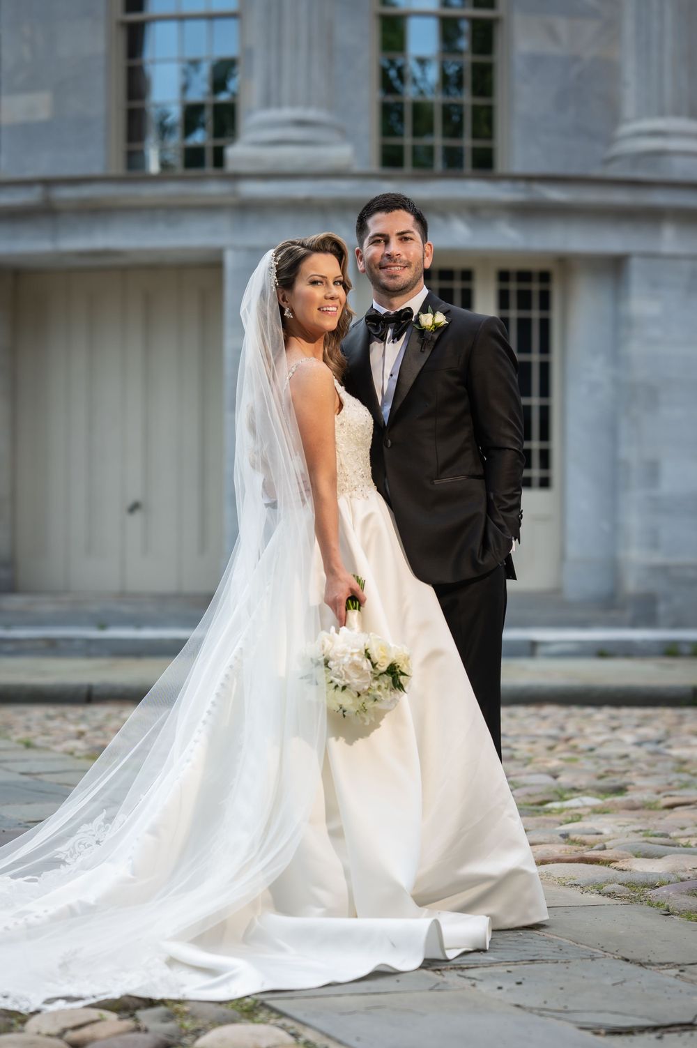Elegant wedding portrait in front of a historic stone building with tall columns.