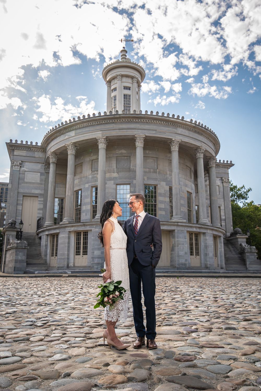 Wedding portrait in front of stately circular building with cobblestone courtyard.