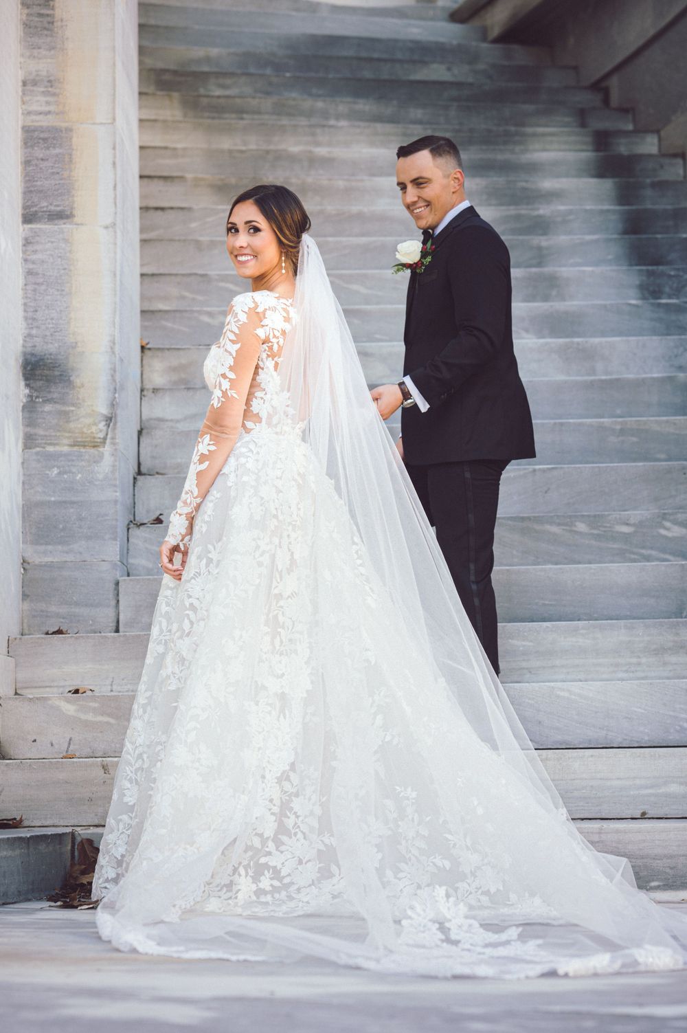 Wedding portrait on stone steps featuring intricate lace gown and long veil.