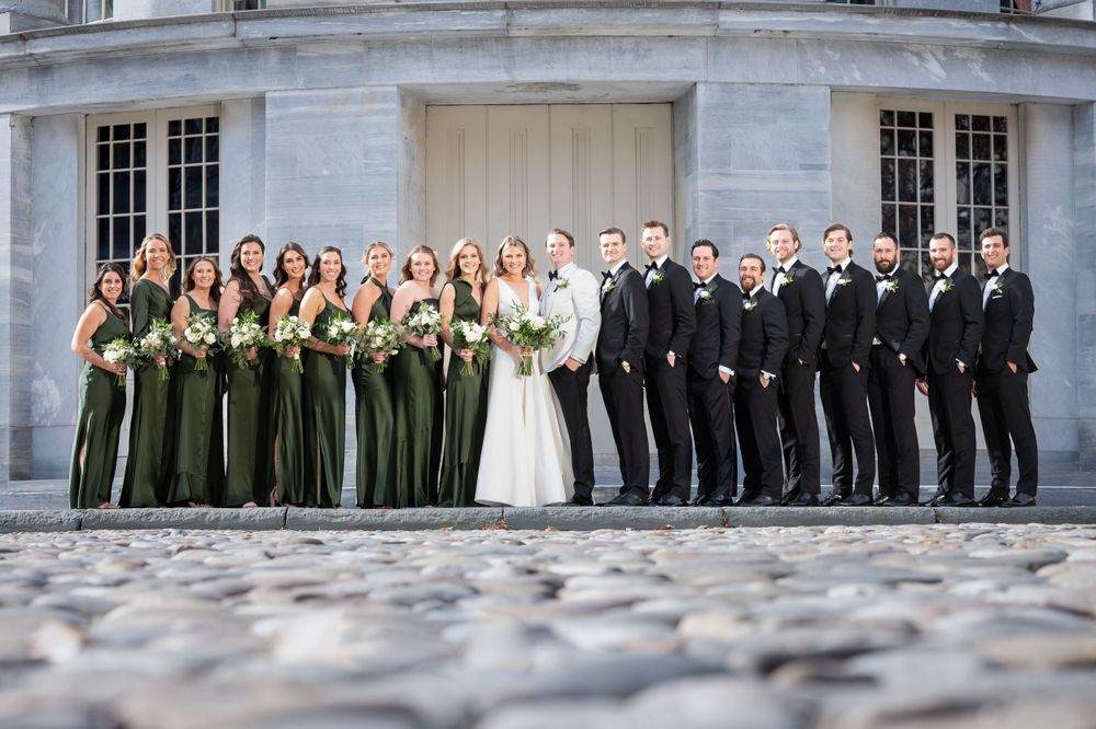 Wedding party in green and black formal attire posed in front of historic building.