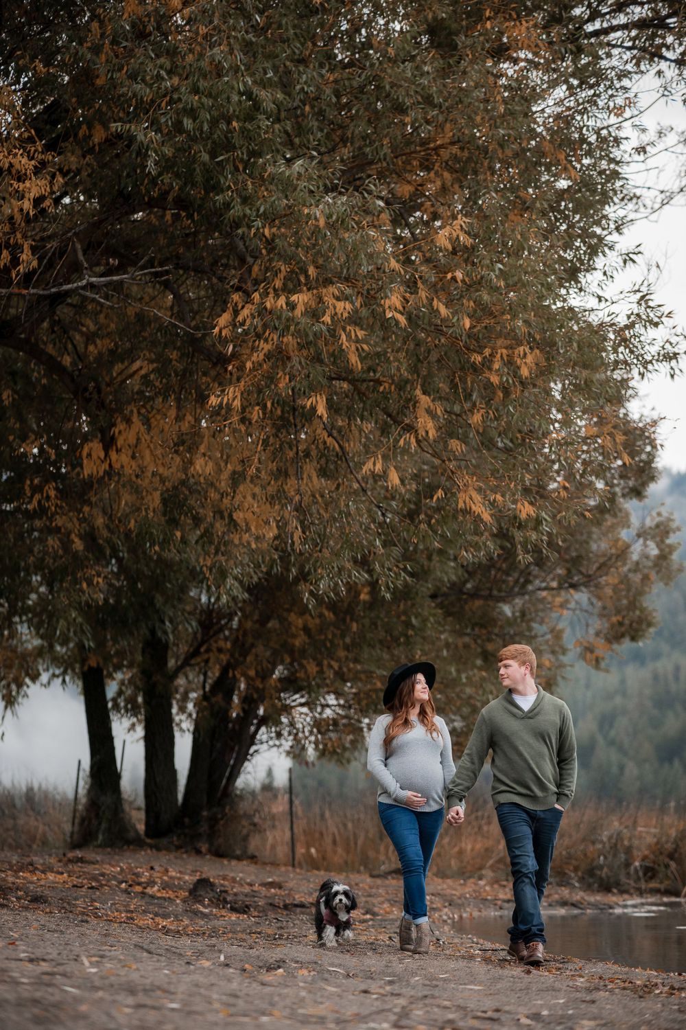 A pregnant couple strolls with their dog in the colorful fall leaves of Spokane Valley during a maternity session.