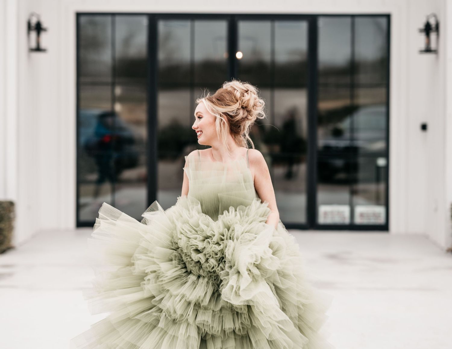 Ethereal sage green tulle gown with dramatic ruffled skirt against modern building.