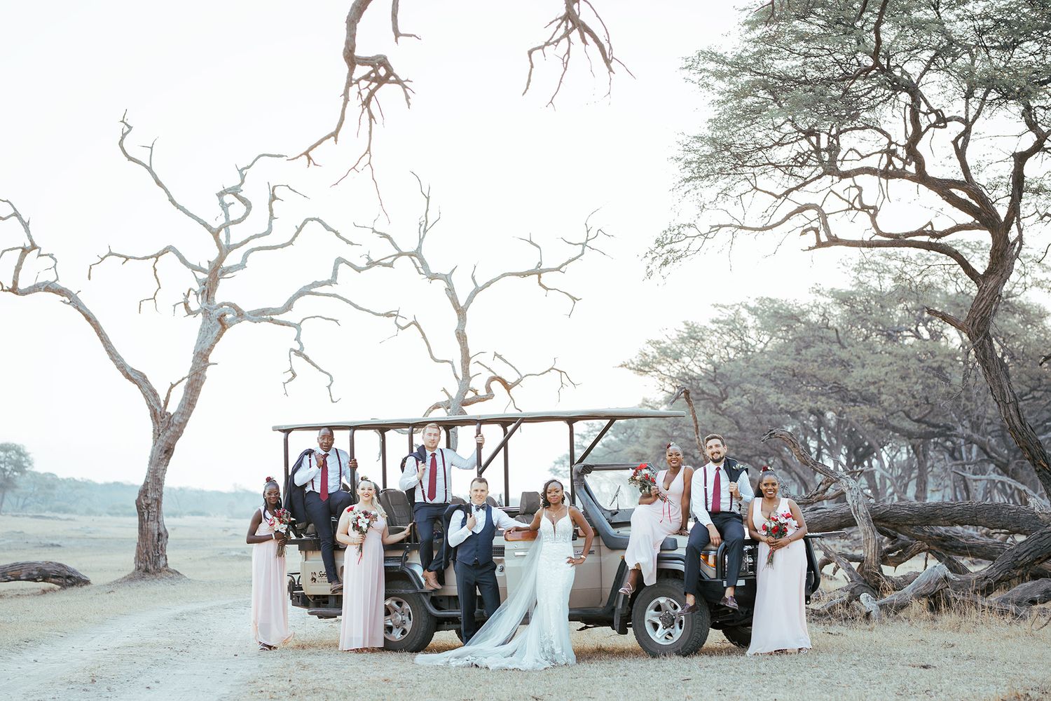 Wedding party poses under barren trees at scenic outdoor location during sunset.