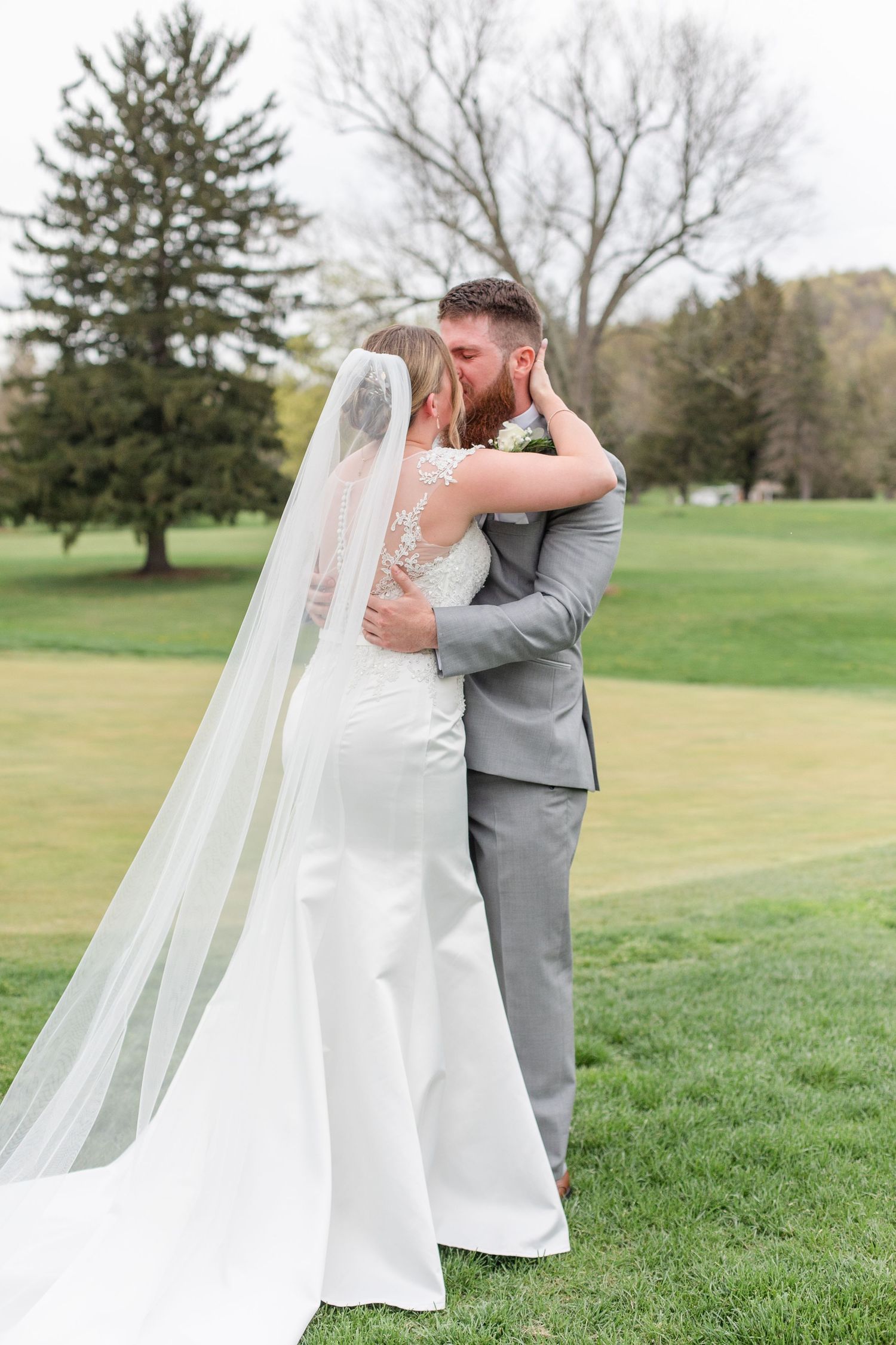 A loving embrace between newlyweds on a scenic golf course with evergreen trees in the background.
