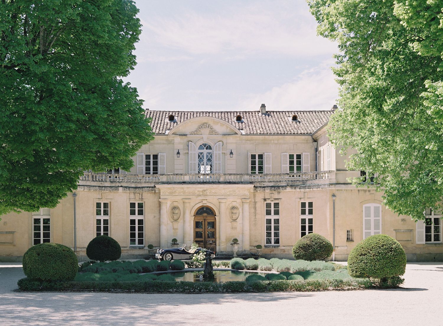 Grand French chateau with symmetrical architecture and manicured gardens featuring a central fountain.