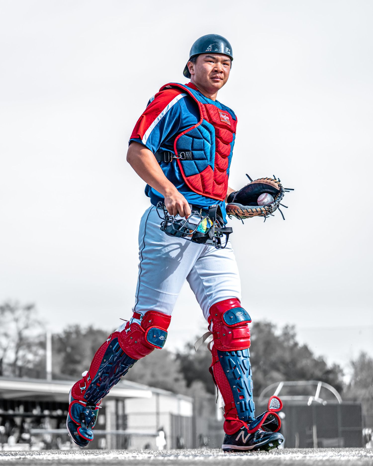 Baseball catcher in red and blue gear showing ready stance with mitt.