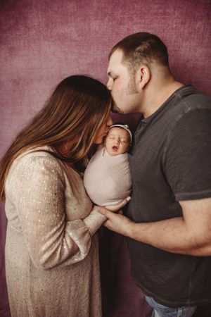 Intimate family portrait session against burgundy backdrop showing tender moments with a newborn.