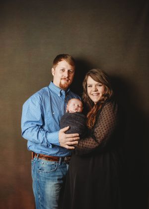 A family portrait against a dark backdrop featuring a baby and parents in casual attire.