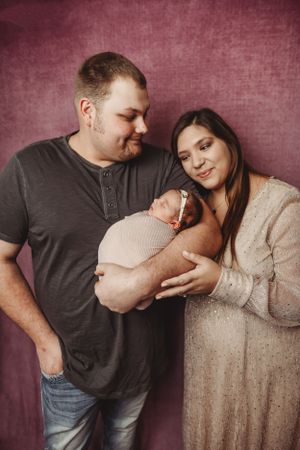 Family portrait series showing parents sharing intimate moments with their newborn against burgundy background.