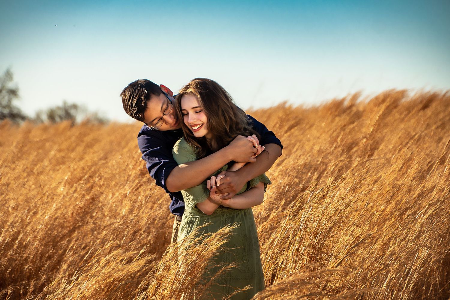 Joyful couple embraces in sunlit golden wheat field during sunset.