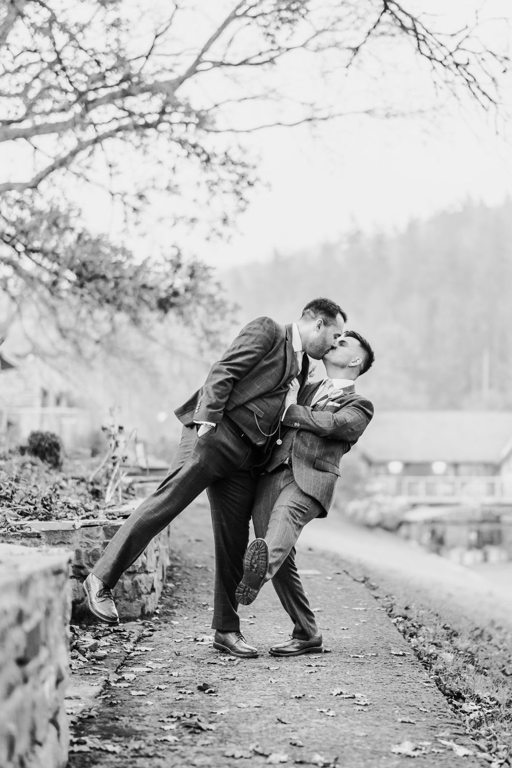 A black and white photo captures two people in suits sharing a playful moment on a path.