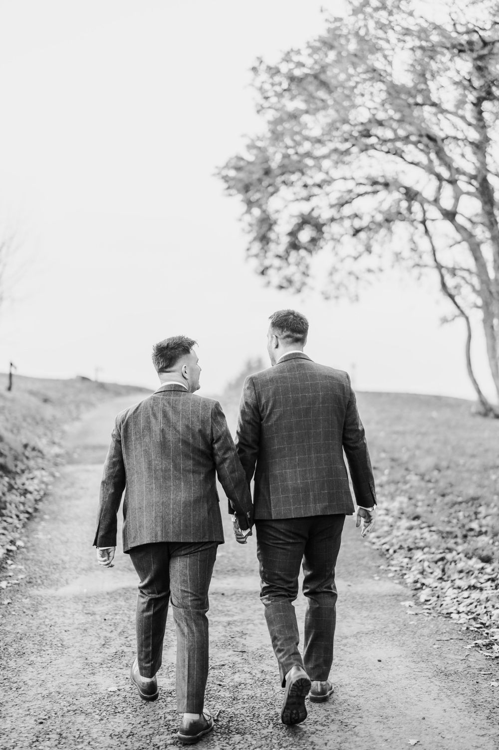 A black and white image shows two people walking hand in hand along a countryside path.