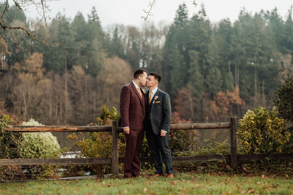A romantic autumn scene with coordinating burgundy and black attire against a backdrop of evergreen trees.