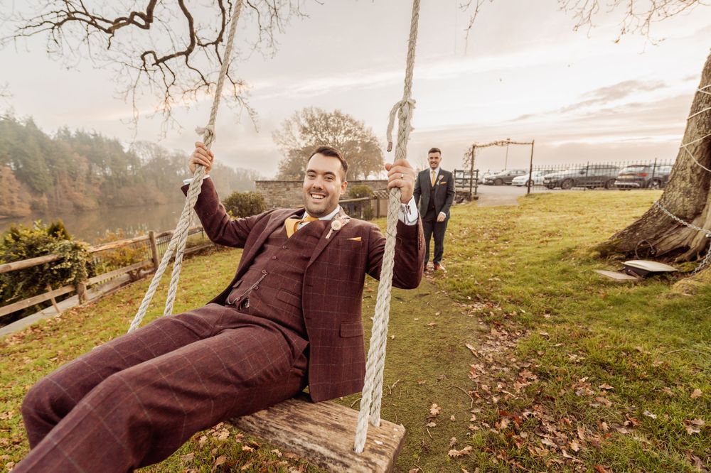 Person in burgundy suit enjoys a wooden swing while another stands in the background.