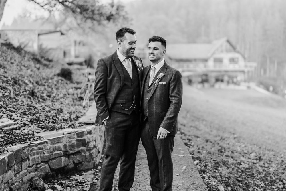 A black and white portrait of two people in suits standing close together on a stone path.