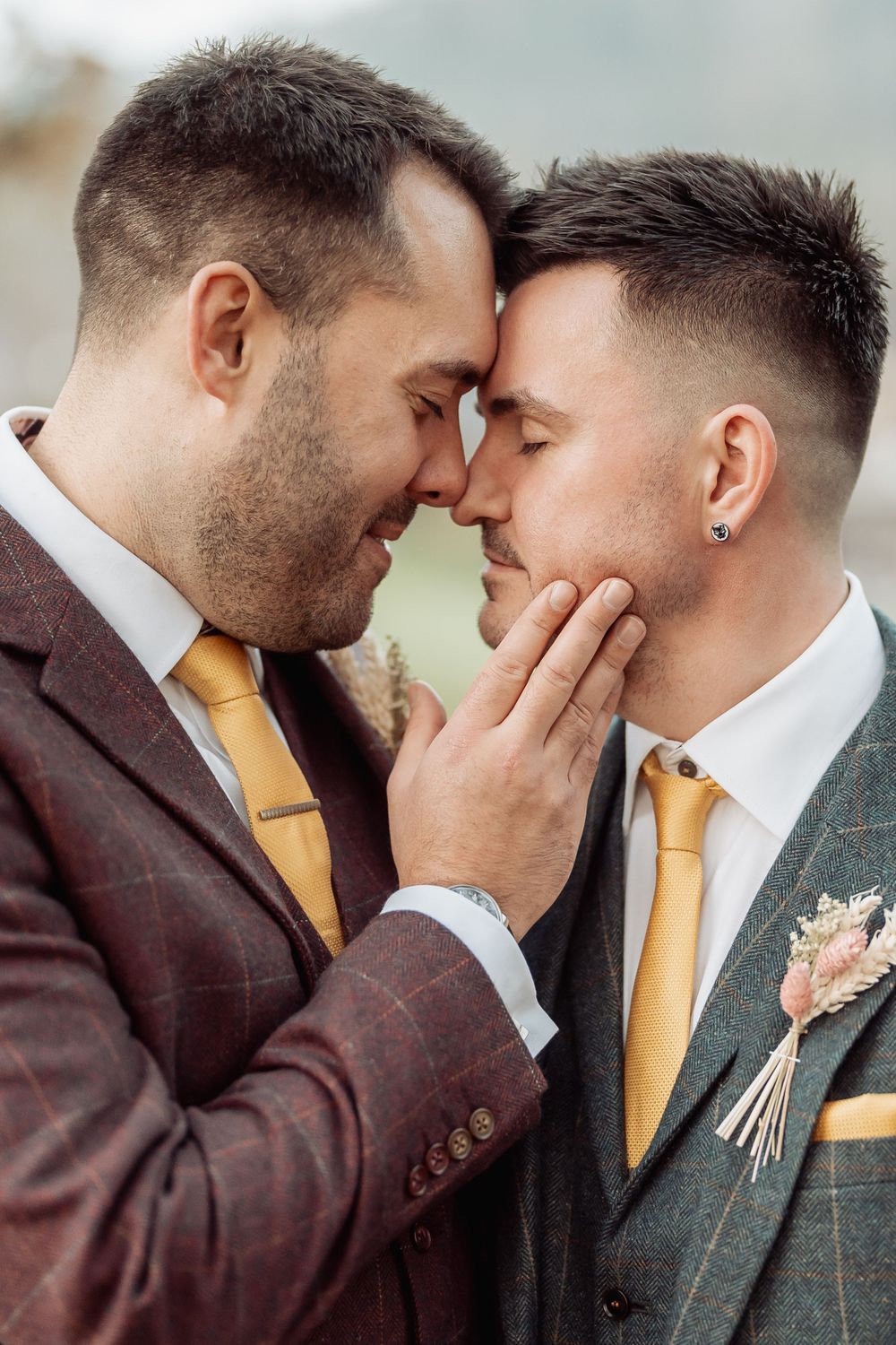 Two people in suits and yellow ties share an intimate moment against a misty background.