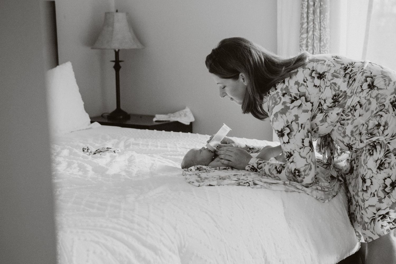 Person in floral dress writing in journal while sitting on white bedding.