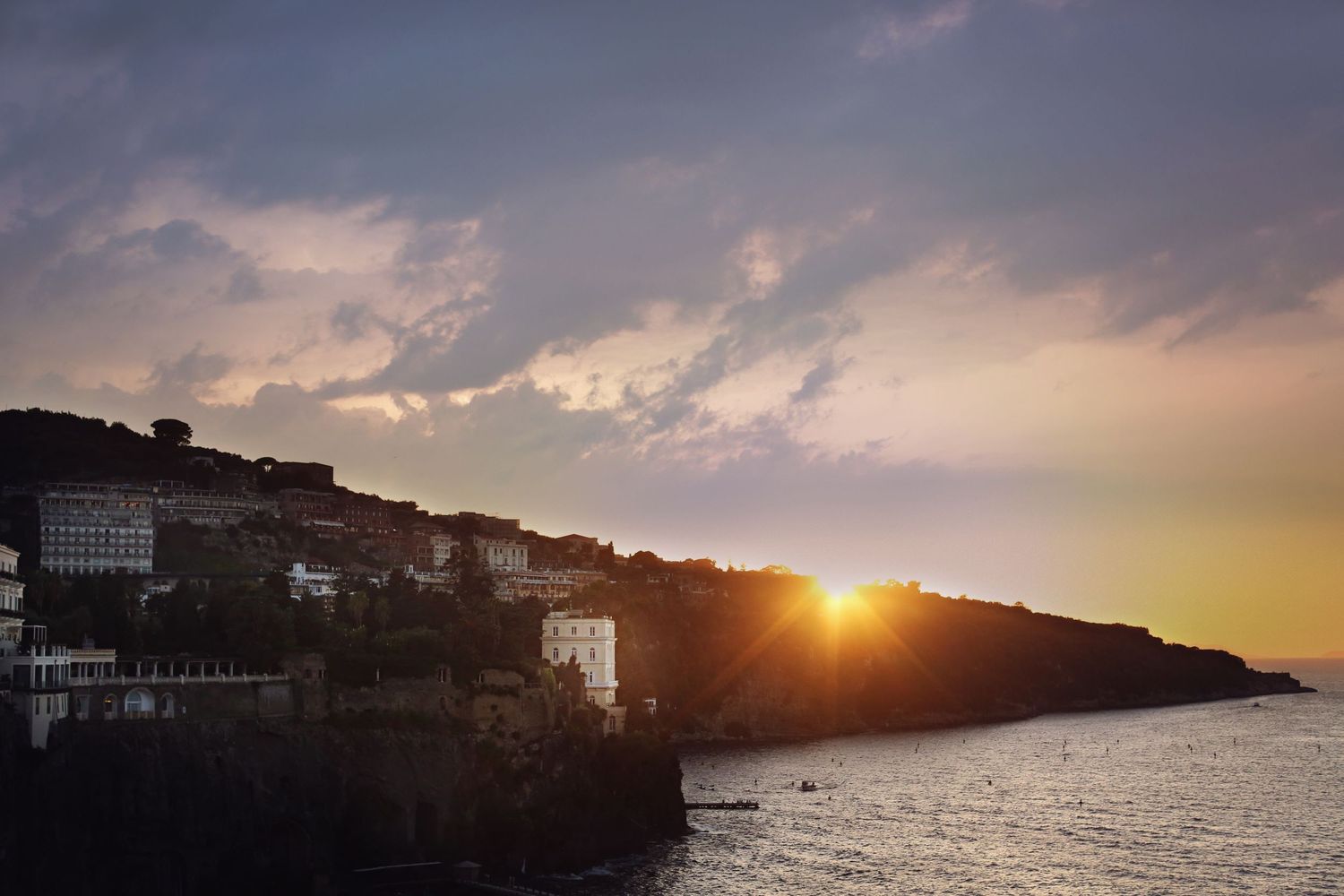 Scenic sunset over coastal buildings and water with dramatic cloudy sky.