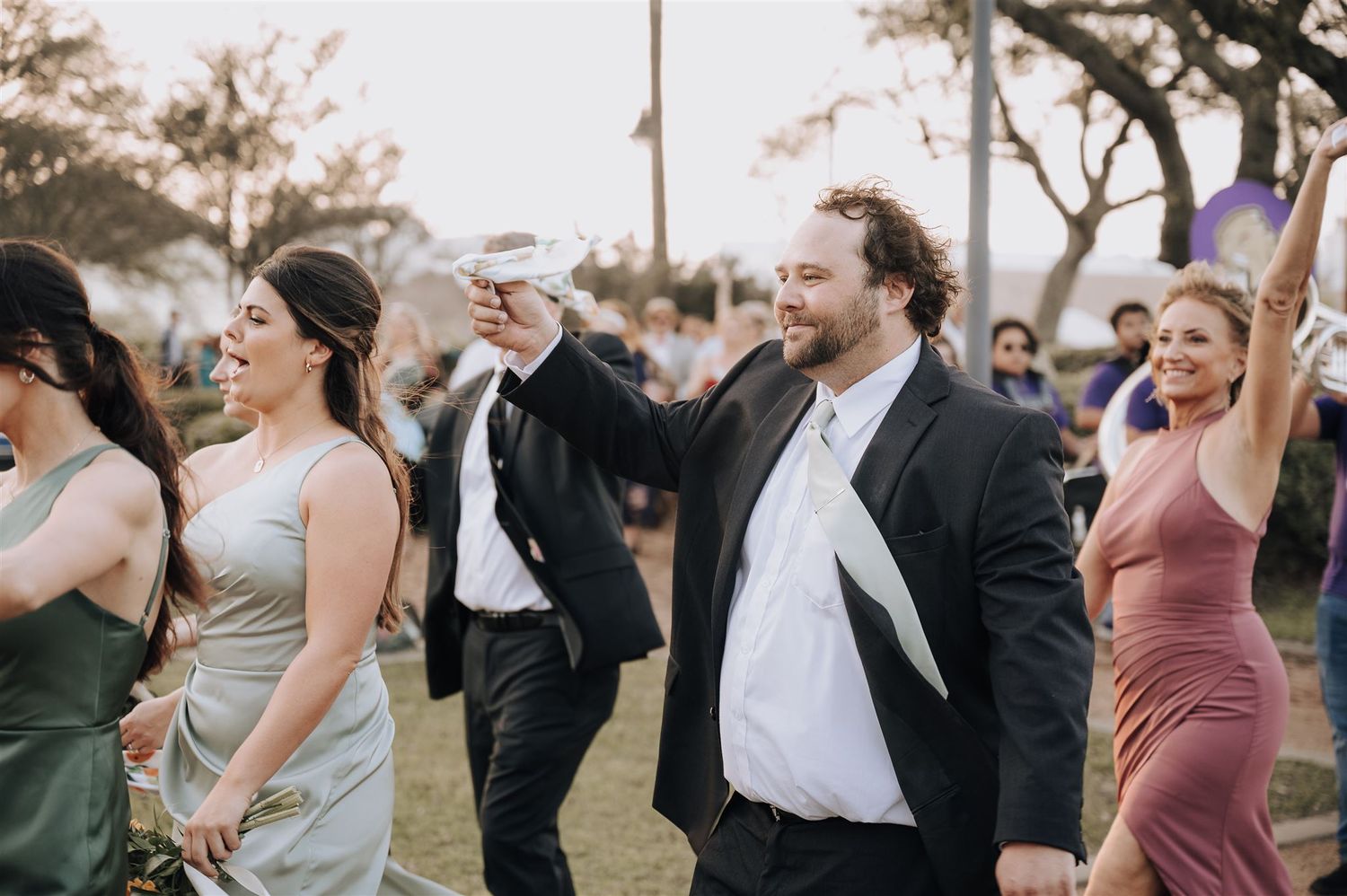 Wedding guests raise their hands in celebration at an outdoor reception.
