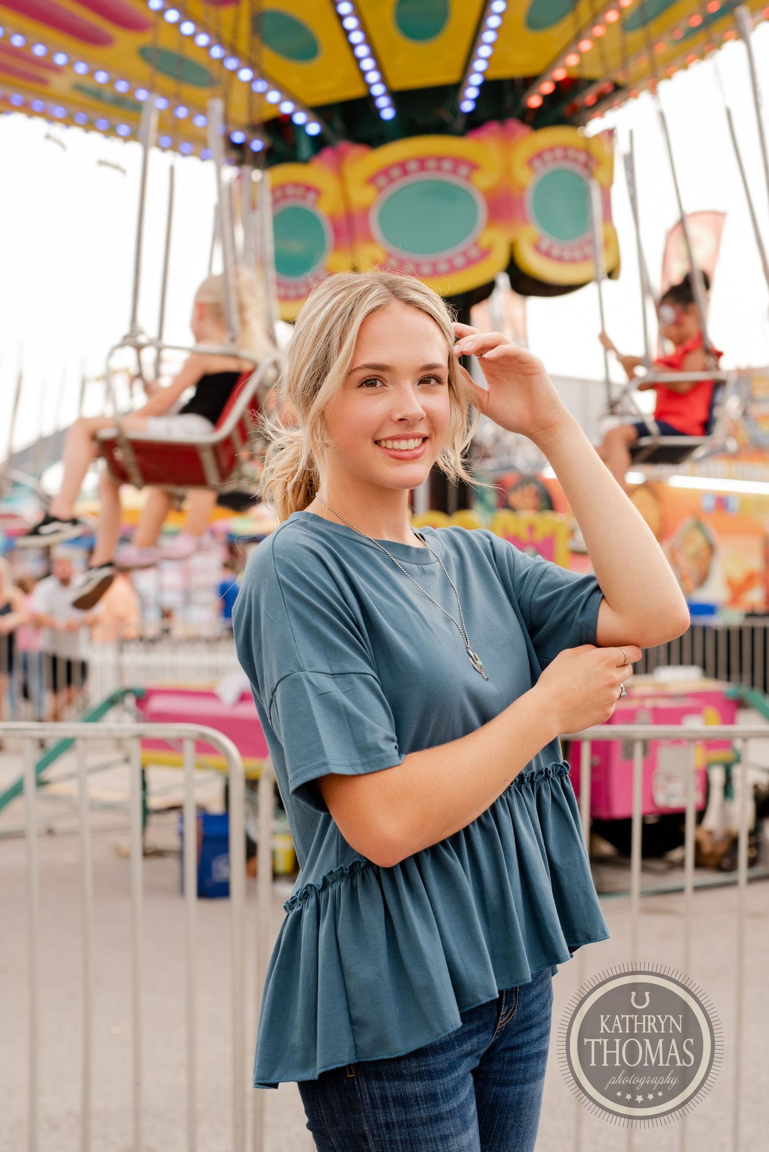 Person in teal ruffle shirt posing in front of vintage carnival ride with twinkling lights.