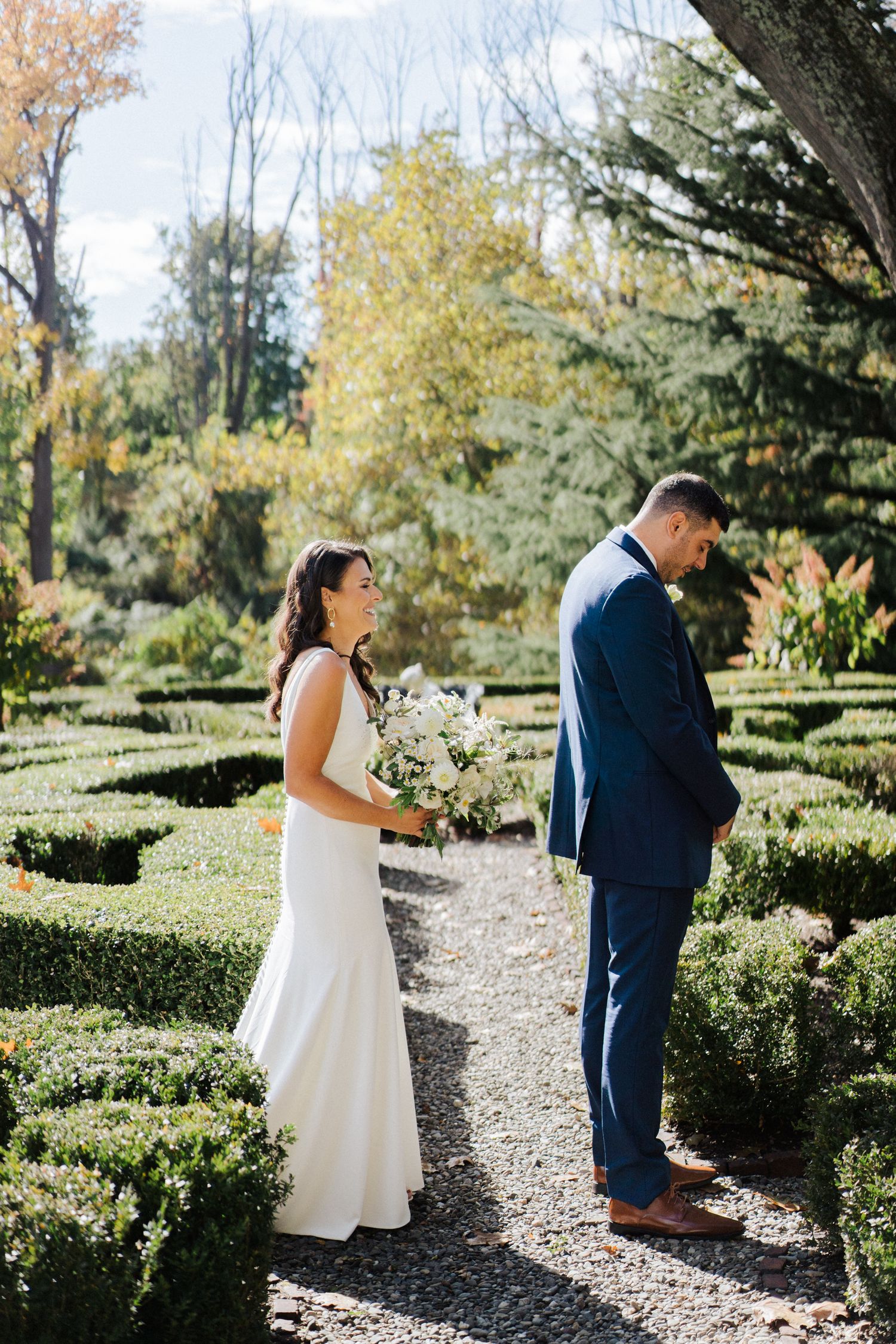 A first look wedding moment on a garden path surrounded by well-maintained hedges and fall colors.