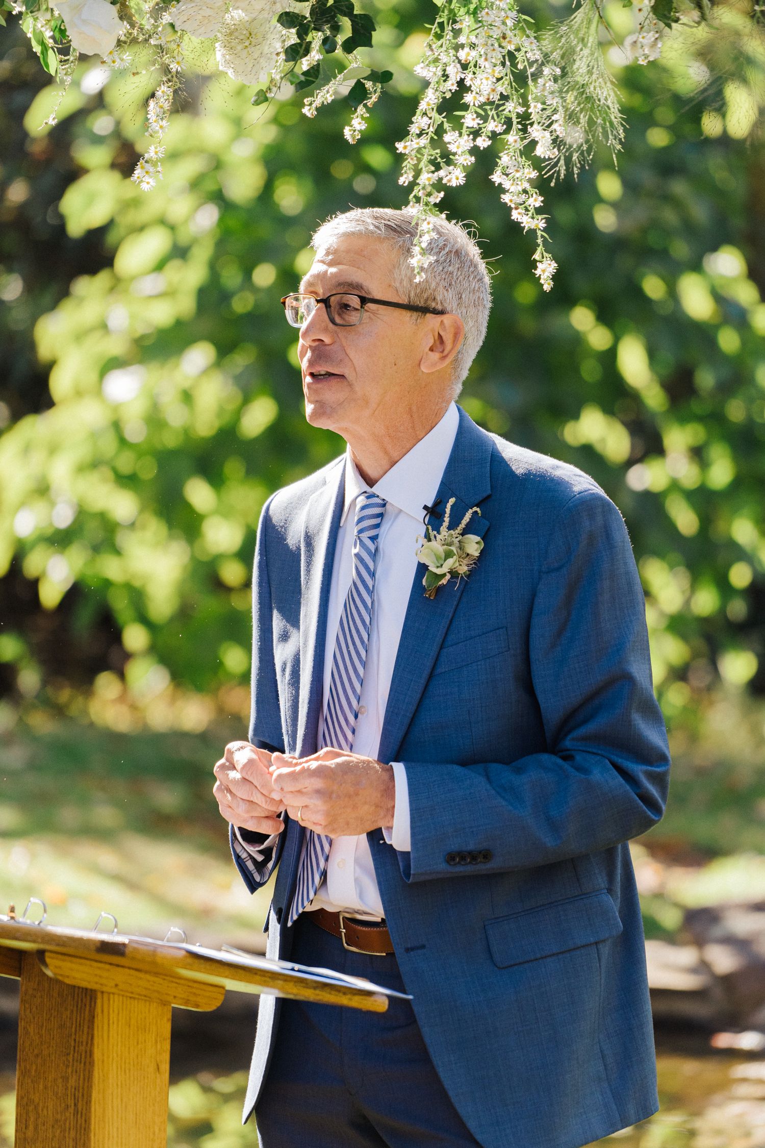 A speaker in a blue suit and striped tie delivers remarks at an outdoor podium.