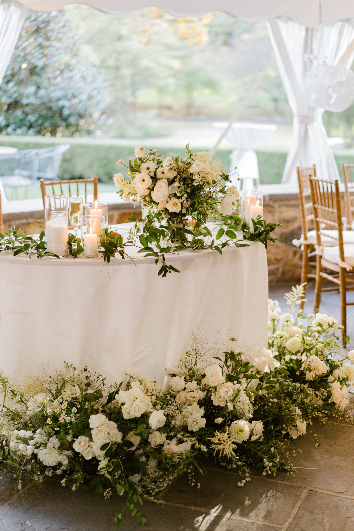 White floral arrangements adorn wedding reception table under tent.