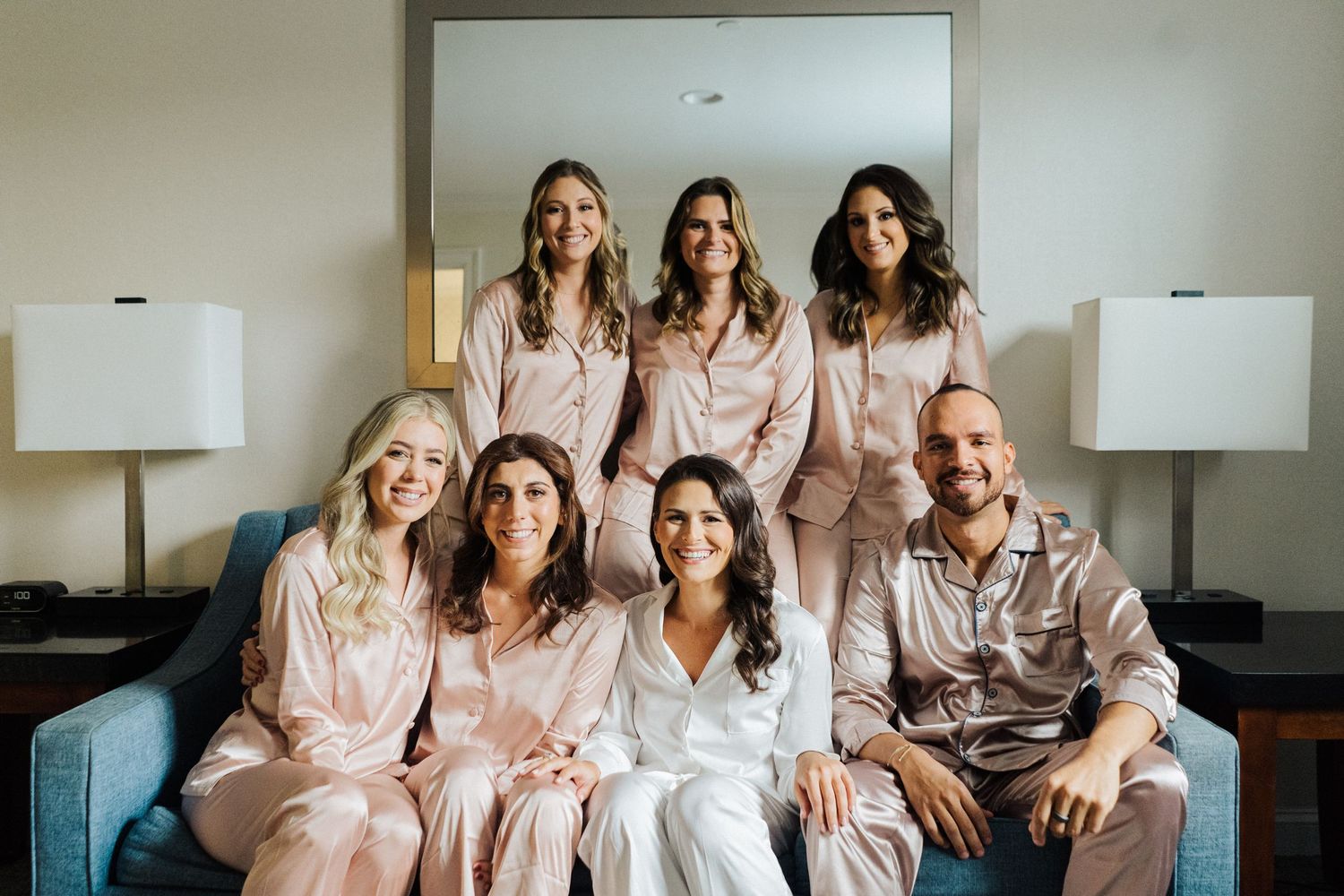 Wedding party members pose on a couch wearing matching pink satin robes.
