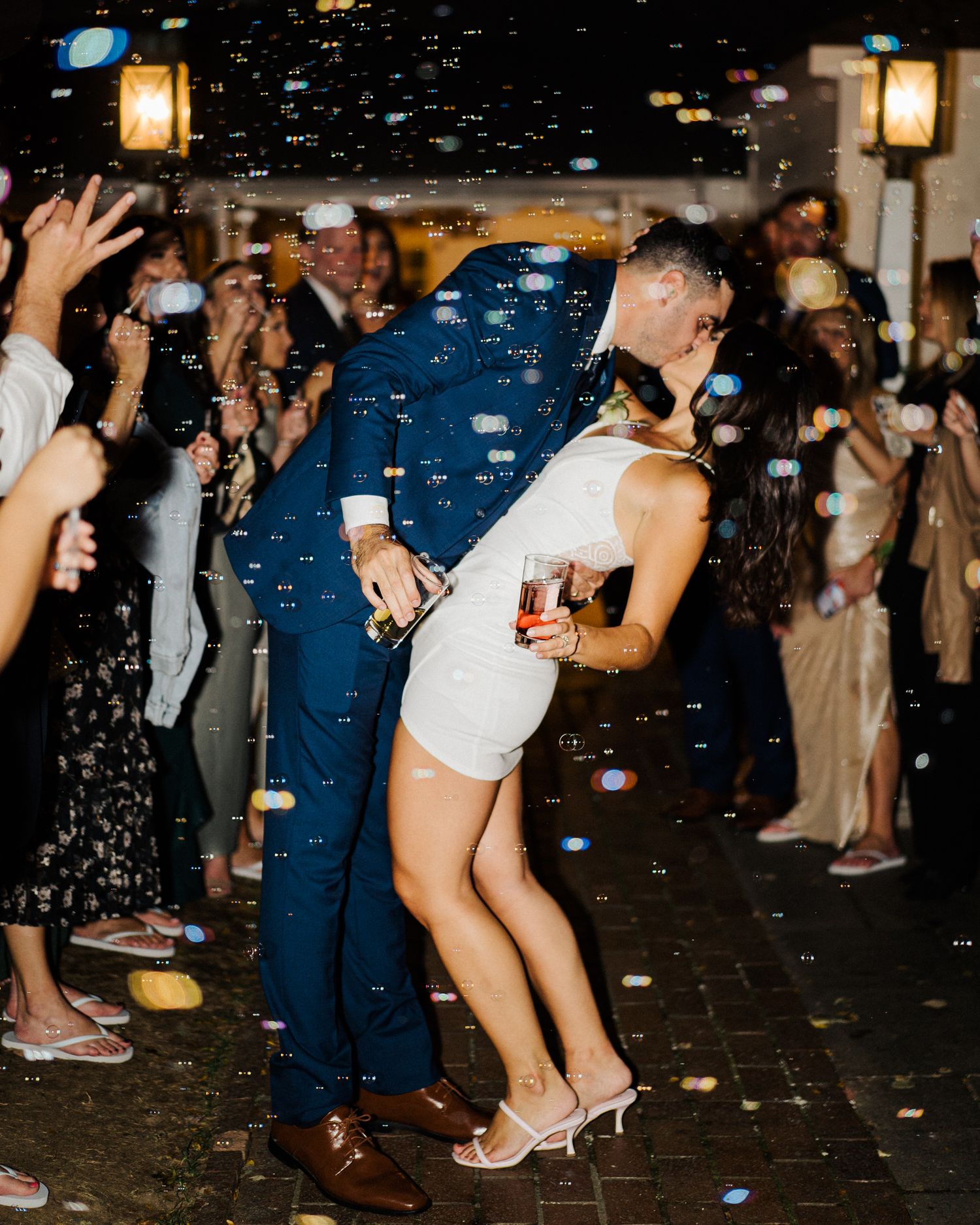 Couple dancing surrounded by bubbles and guests at nighttime celebration.