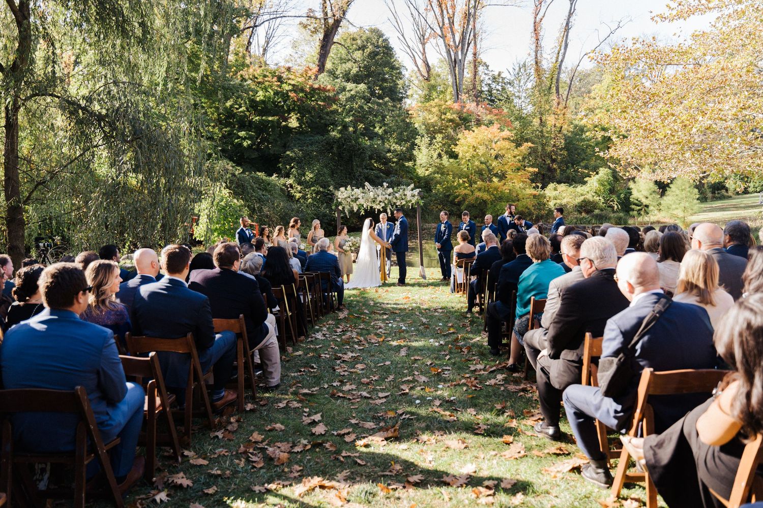 A wide view of an outdoor wedding ceremony with rows of guests seated in a garden setting.