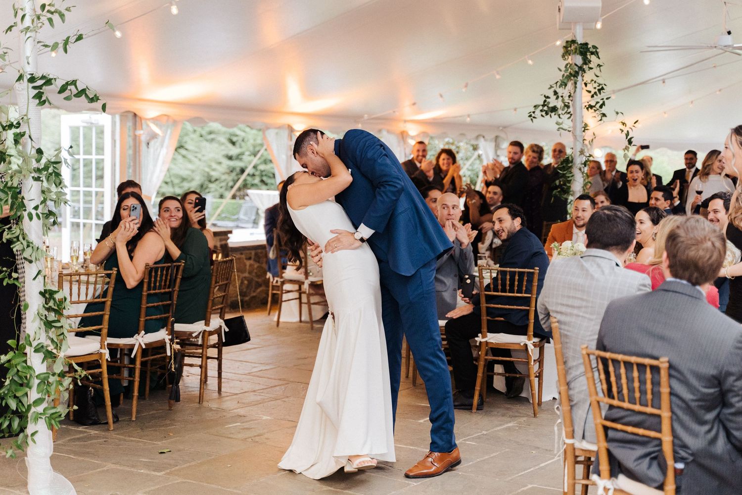 A couple shares their first dance in a beautifully decorated tent venue with guests watching from golden chairs.