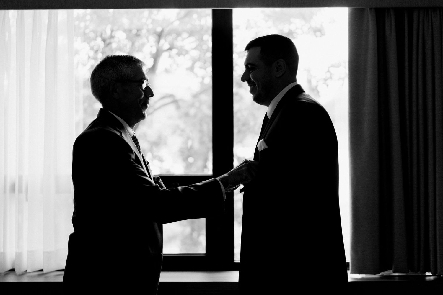 Silhouette of two people in formal wear talking by a window.