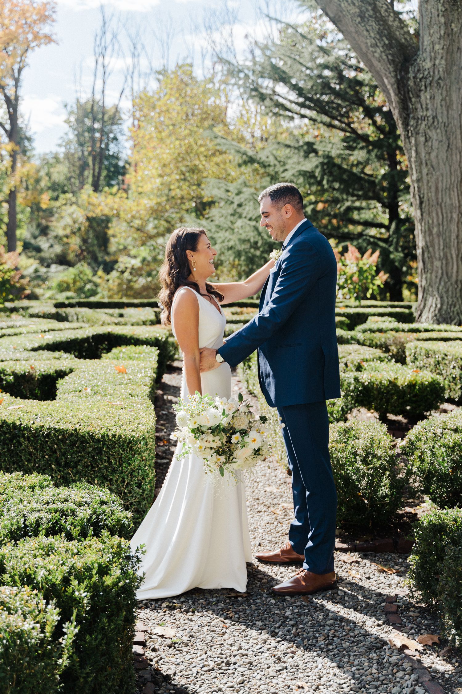 A couple embraces in a sunlit garden with beautiful hedges and autumn foliage.