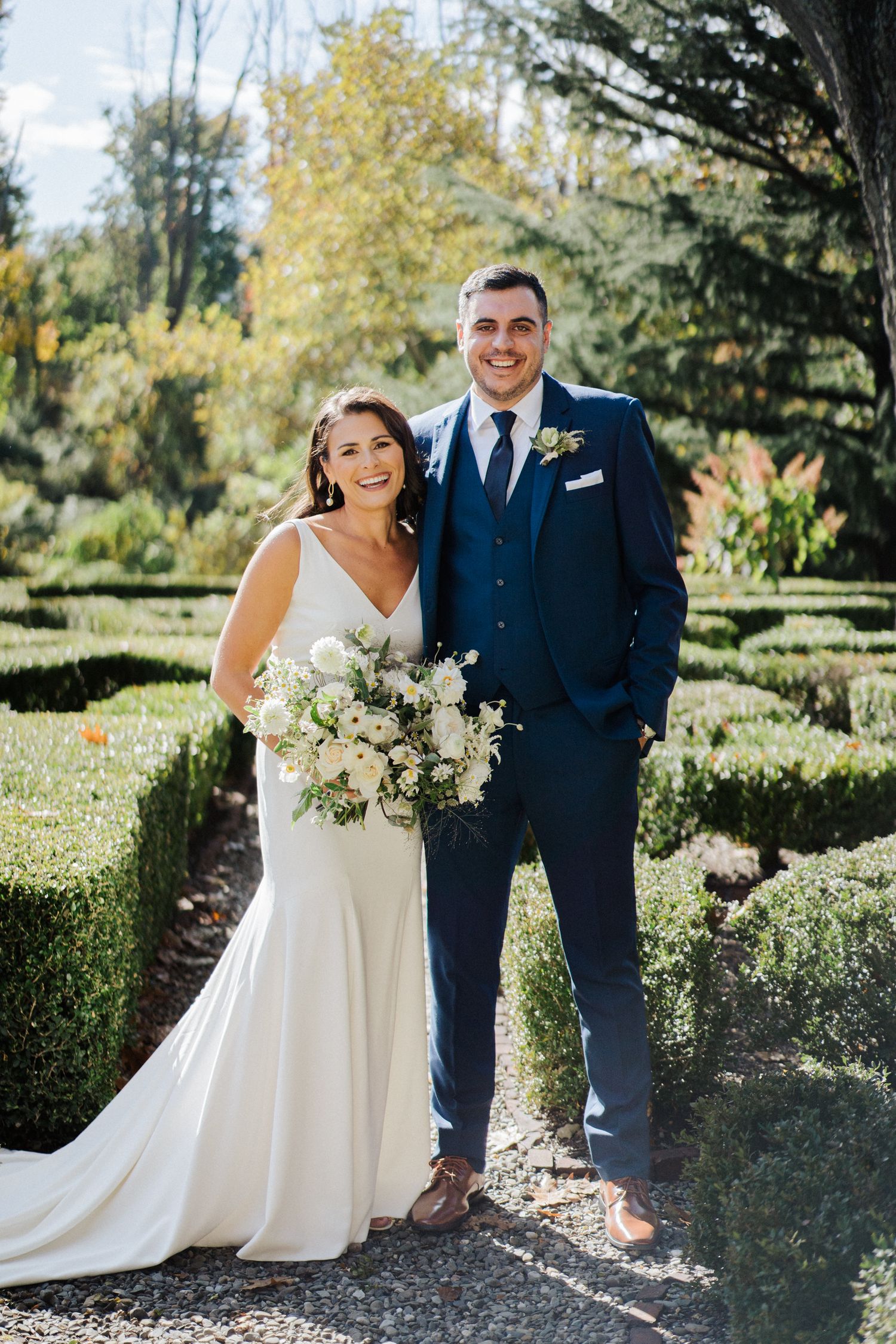 A sunny wedding portrait in a beautiful garden setting with perfectly manicured hedges and fall foliage.