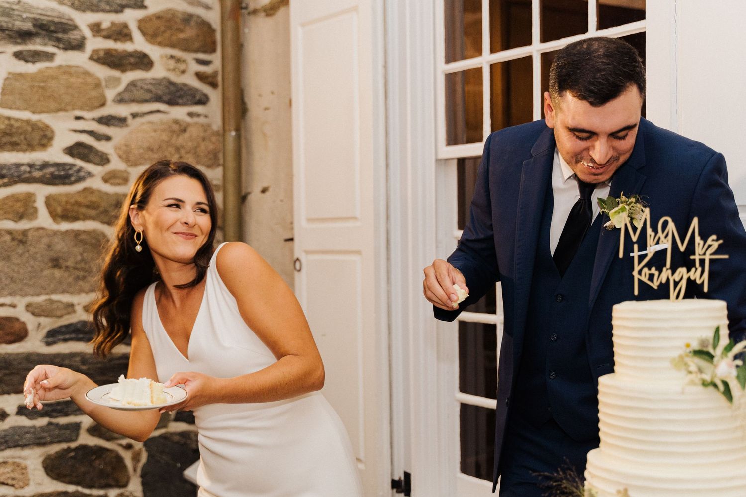 Couple laughing while feeding each other wedding cake at their reception.