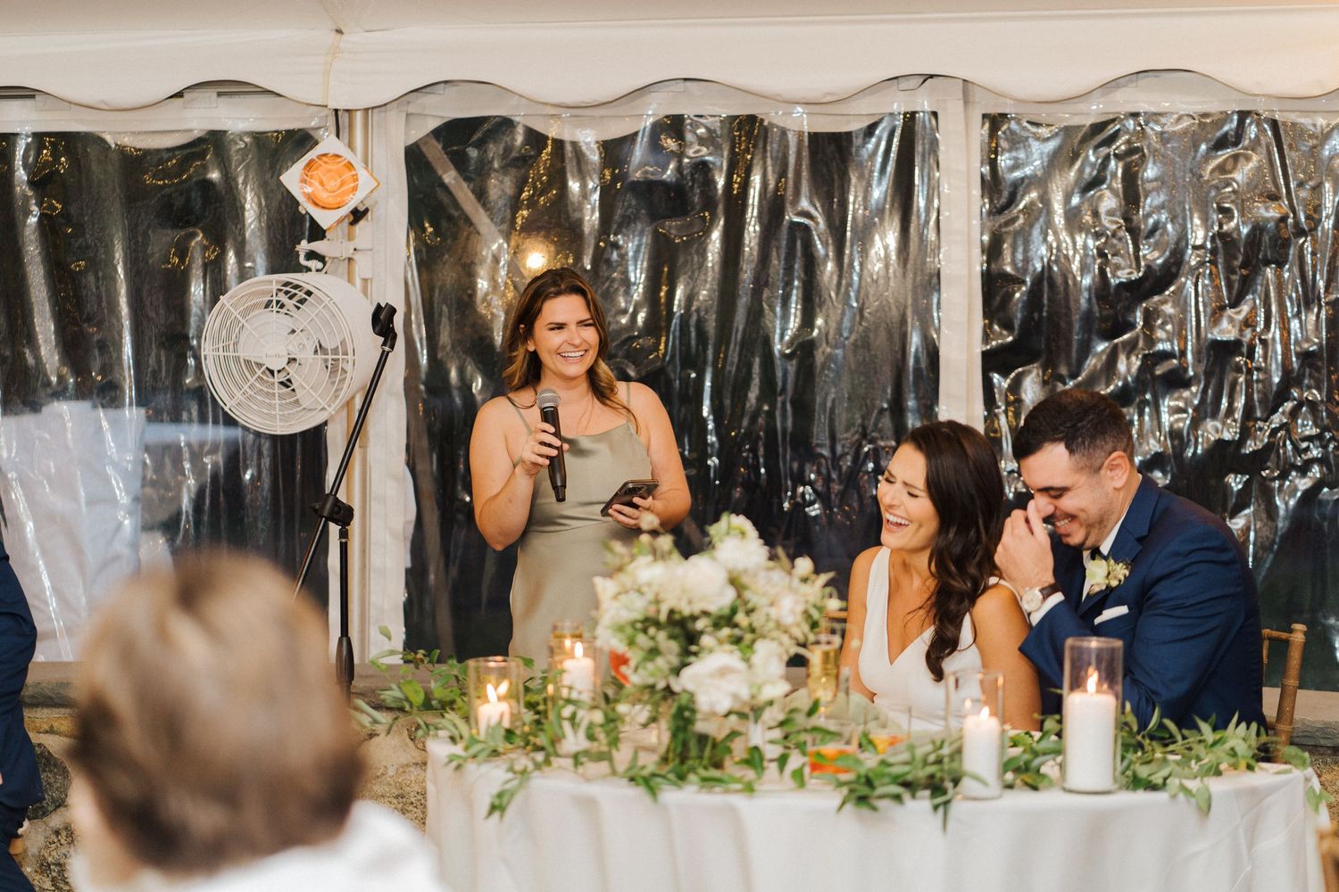 A wedding guest gives a speech while standing at the reception head table.
