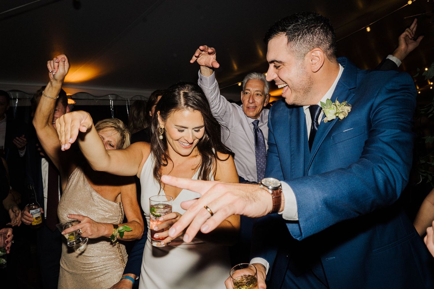 Wedding celebration on dance floor with guests dancing energetically under tent lighting.