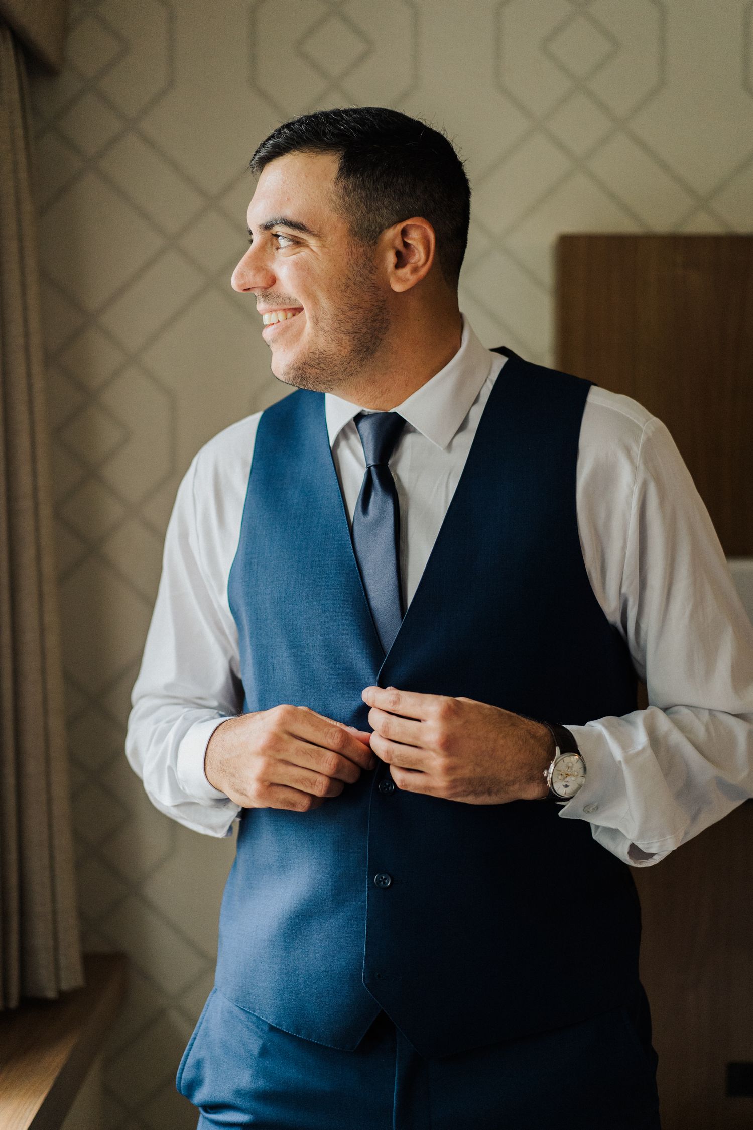 Side profile of person in blue vest and white shirt adjusting clothing while smiling.