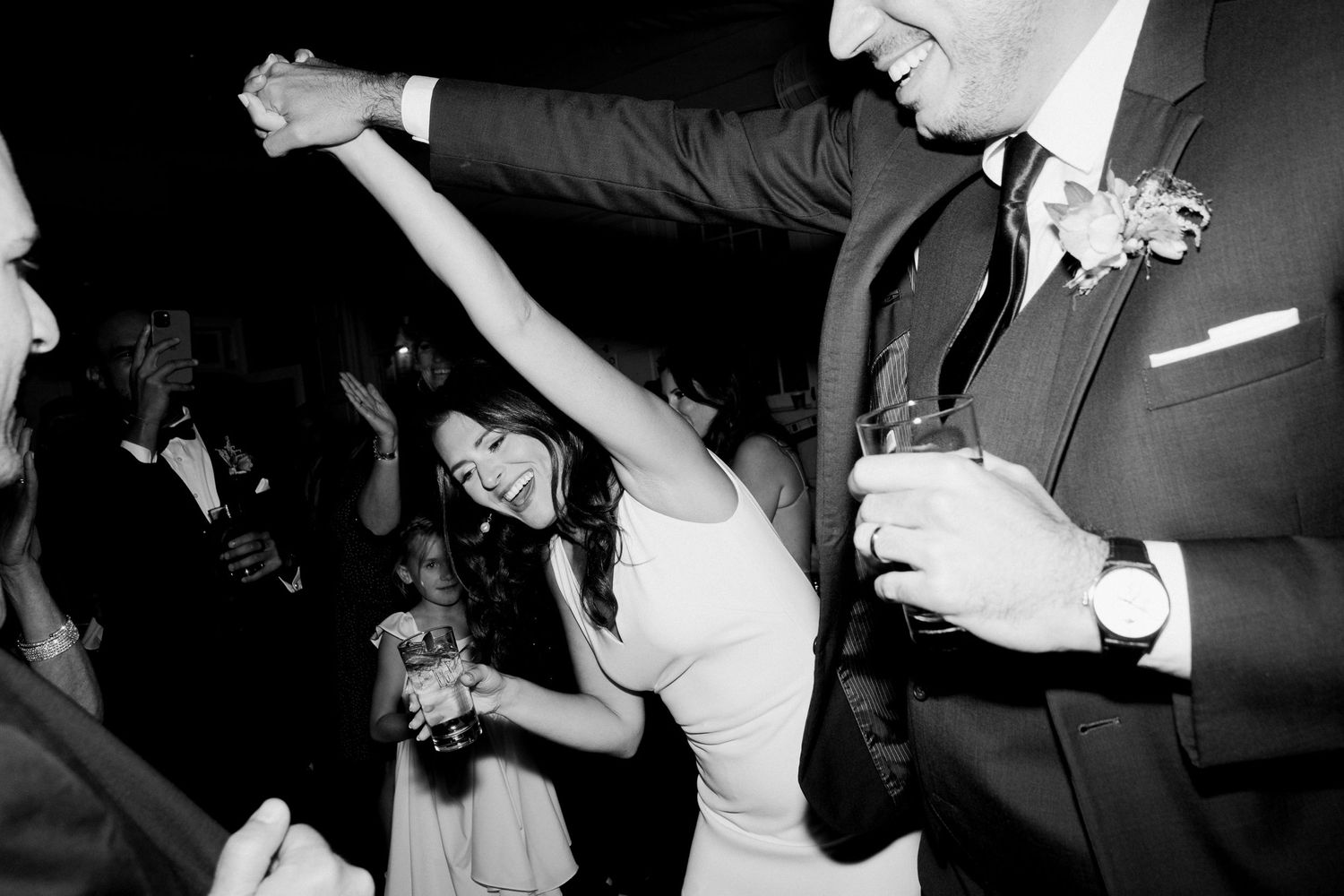Wedding guests dance and celebrate joyfully on a dance floor at a reception in black and white.
