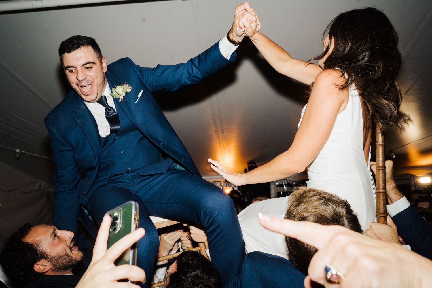 Newlyweds celebrate on the dance floor as guests lift them up during reception party.
